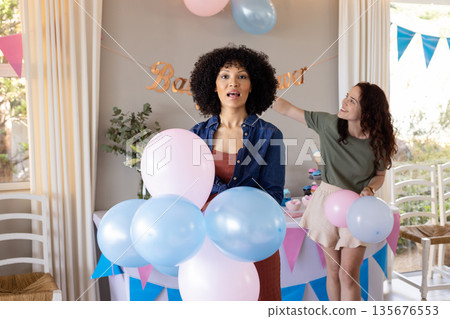 Women decorating for baby shower, holding pastel balloons and smiling joyfully Women decorating for baby shower, holding pastel balloons and smiling joyfully 135676553