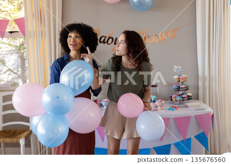 Decorating for baby shower, women arranging balloons and cupcakes in festive setting 135676560