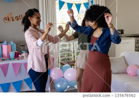 Friends celebrating at home, dancing joyfully with colorful balloons and decorations 135676562