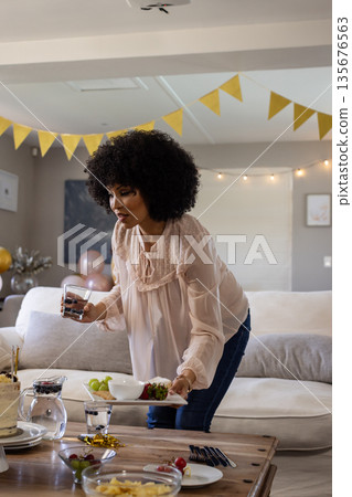 Woman preparing snacks and drinks for celebration at home, smiling warmly Woman preparing snacks and drinks for celebration at home, smiling warmly 135676563