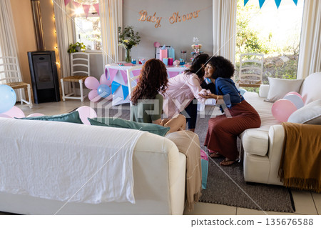 Friends celebrating baby shower at home, hugging and smiling with decorations around Friends celebrating baby shower at home, hugging and smiling with decorations around 135676588