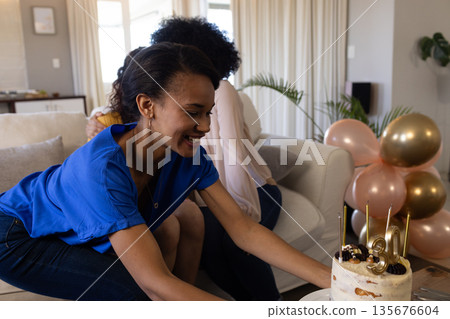 Smiling woman placing birthday cake on table during celebration at home 135676604