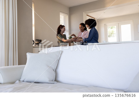 Women exchanging gifts and smiling in modern living room, celebrating together 135676616