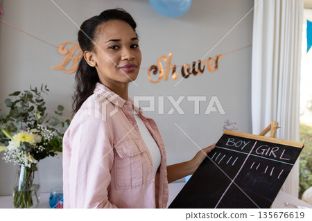 Smiling woman holding chalkboard at baby shower, enjoying festive celebration Smiling woman holding chalkboard at baby shower, enjoying festive celebration 135676619