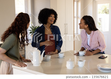 Pregnant woman in kitchen enjoying conversation with friends over coffee Pregnant woman in kitchen enjoying conversation with friends over coffee 135676621