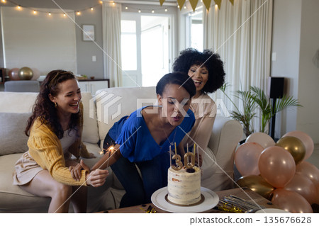 Celebrating birthday, woman blowing candles on cake with friends at home Celebrating birthday, woman blowing candles on cake with friends at home 135676628