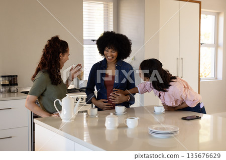 Friends celebrating pregnancy in kitchen, smiling and enjoying tea together Friends celebrating pregnancy in kitchen, smiling and enjoying tea together 135676629