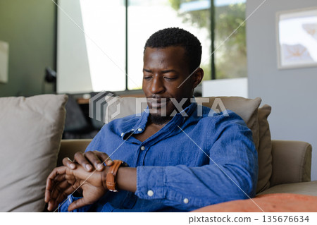Relaxing at home, man checking time on wristwatch, enjoying leisure moment 135676634