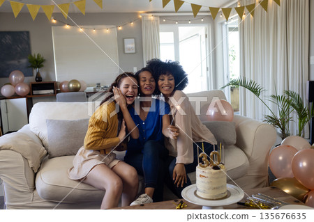 Friends celebrating birthday at home, smiling and holding sparklers on sofa 135676635