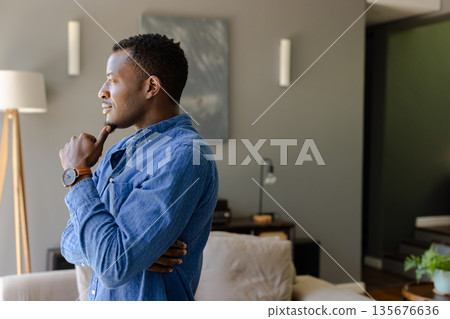 Thoughtful man in blue shirt contemplating at home, looking out window Thoughtful man in blue shirt contemplating at home, looking out window 135676636