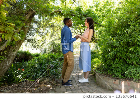 Couple holding hands and smiling in lush garden, enjoying romantic moment together Couple holding hands and smiling in lush garden, enjoying romantic moment together 135676641