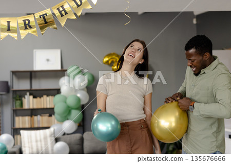 Celebrating birthday at home, friends inflating balloons with festive decorations Celebrating birthday at home, friends inflating balloons with festive decorations 135676666