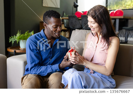 Couple exchanging gift on sofa, smiling and enjoying special moment together 135676667