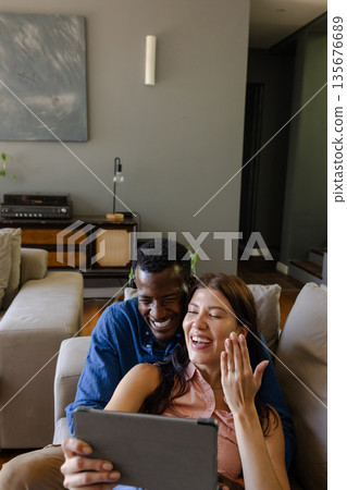 Couple laughing while video chatting on tablet at home, enjoying quality time 135676689