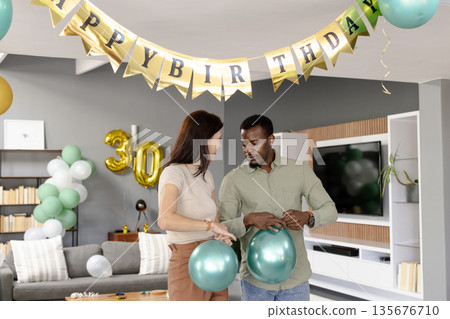 Couple decorating living room with balloons for birthday celebration at home Couple decorating living room with balloons for birthday celebration at home 135676710