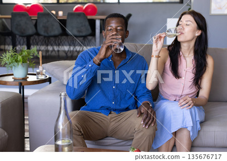 Couple enjoying drinks together on sofa, celebrating at home with champagne 135676717