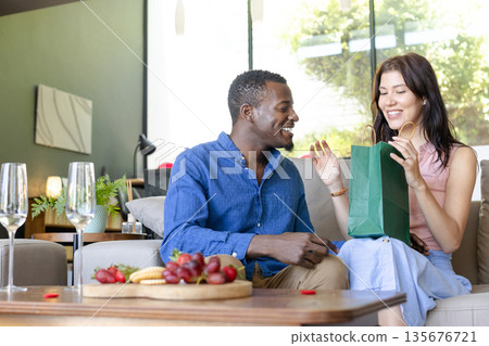 Couple exchanging gifts at home, smiling and enjoying joyful celebration Couple exchanging gifts at home, smiling and enjoying joyful celebration 135676721