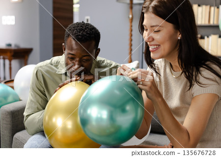 Friends inflating colorful balloons, preparing for festive celebration at home Friends inflating colorful balloons, preparing for festive celebration at home 135676728
