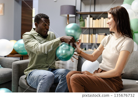 Friends playing with balloons and laughing together in cozy living room 135676732
