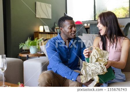 Couple exchanging gifts on sofa, smiling and enjoying joyful celebration Couple exchanging gifts on sofa, smiling and enjoying joyful celebration 135676743