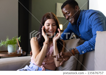 Happy couple exchanging gifts on cozy sofa, sharing joyful surprise and laughter 135676757