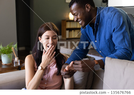 Man proposing to surprised woman at home, both smiling and joyful 135676766