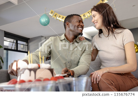 Couple celebrating birthday at home, smiling and enjoying cake together 135676774