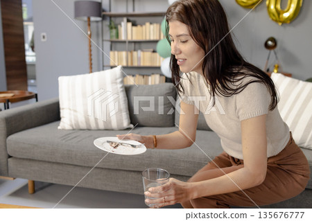 Woman cleaning up after party at home, holding plate and glass, smiling Woman cleaning up after party at home, holding plate and glass, smiling 135676777