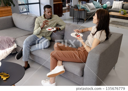 Friends enjoying dessert and conversation on cozy living room sofa Friends enjoying dessert and conversation on cozy living room sofa 135676779