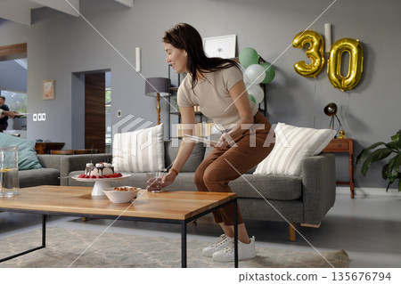 Woman preparing table with cake and snacks for birthday celebration at home Woman preparing table with cake and snacks for birthday celebration at home 135676794