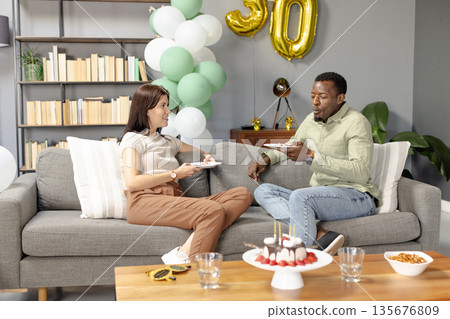 Celebrating birthday, friends sharing cake and chatting on cozy living room sofa 135676809