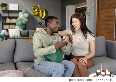 Celebrating birthday, African American man giving gift to woman on living room sofa Celebrating birthday, African American man giving gift to woman on living room sofa 135676810