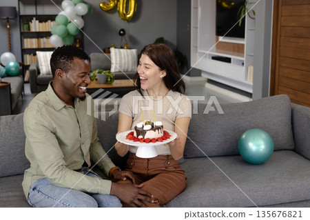 Celebrating birthday, African American man and woman smiling with cake on sofa 135676821