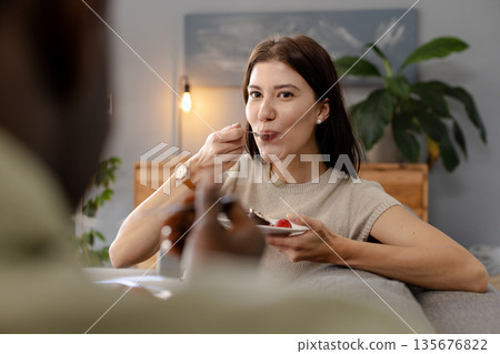 Woman enjoying dessert at home, smiling and looking content while eating 135676822