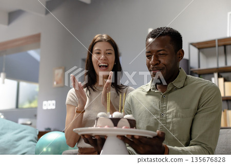 Celebrating birthday, happy couple enjoying cake with candles at home Celebrating birthday, happy couple enjoying cake with candles at home 135676828