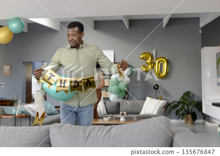 African American man decorating living room with birthday banner for celebration 135676847