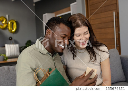 African American man and woman exchanging gifts on couch, both smiling happily African American man and woman exchanging gifts on couch, both smiling happily 135676851