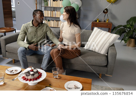 Couple sitting on sofa holding hands, celebrating with cake in living room Couple sitting on sofa holding hands, celebrating with cake in living room 135676854