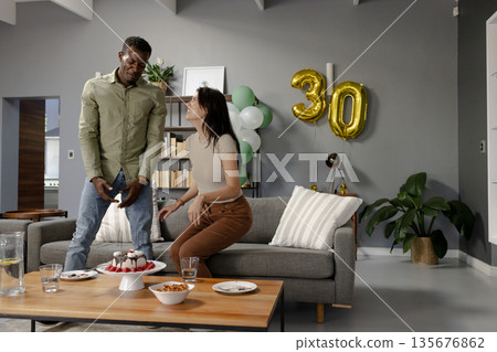 Celebrating 30th birthday, friends enjoying cake and snacks in modern living room Celebrating 30th birthday, friends enjoying cake and snacks in modern living room 135676862