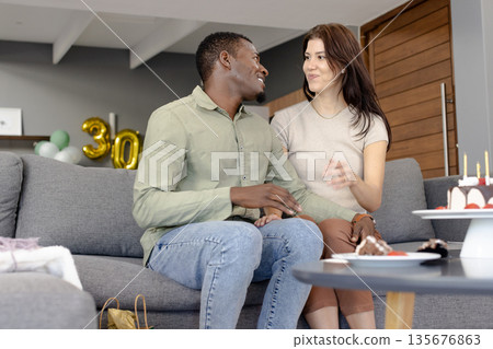 Celebrating birthday on couch, African American man and woman smiling with cake 135676863