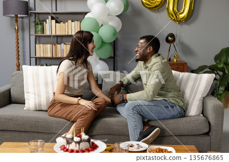 African American man and woman laughing together on sofa during birthday celebration African American man and woman laughing together on sofa during birthday celebration 135676865