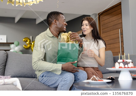 Couple exchanging gifts on sofa, smiling and celebrating birthday at home Couple exchanging gifts on sofa, smiling and celebrating birthday at home 135676870