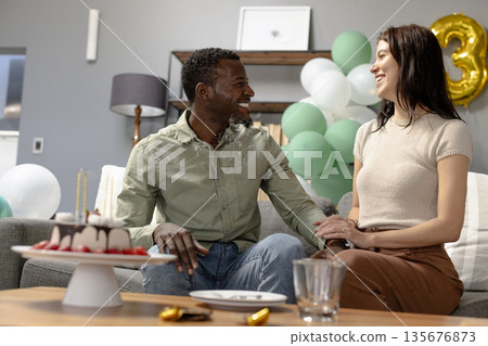 Couple celebrating birthday at home, smiling and enjoying cake on sofa 135676873