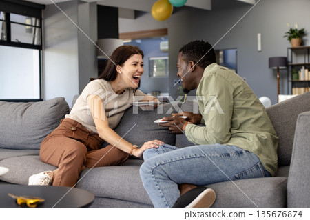 Laughing together, friends enjoying conversation on couch at home with tablets 135676874