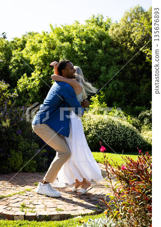Couple joyfully dancing together in sunny garden, surrounded by lush greenery Couple joyfully dancing together in sunny garden, surrounded by lush greenery 135676893