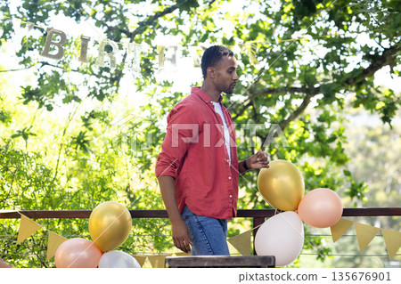 Man in red shirt enjoying outdoor birthday party with festive balloons 135676901