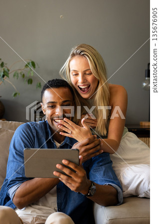 Couple sitting on couch joyfully watching tablet, sharing exciting moment together Couple sitting on couch joyfully watching tablet, sharing exciting moment together 135676905