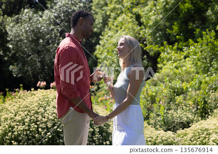 Couple celebrating outdoors, holding champagne glasses and smiling in garden 135676914