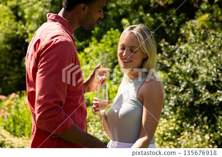 Couple enjoying champagne in sunny garden, celebrating special moment together Couple enjoying champagne in sunny garden, celebrating special moment together 135676918