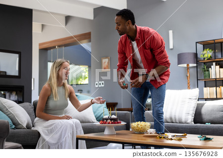 African American man serving cake to smiling woman during home celebration 135676928